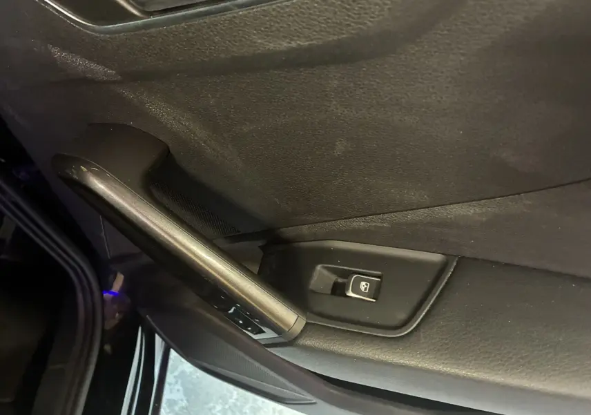 Détail de la porte côté conducteur d’un Audi Q2 noir 2023, avec commande de lève-vitre électrique et poignée intégrée.