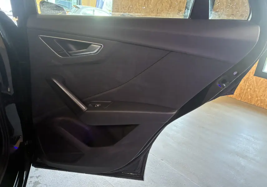 Vue rapprochée de la porte arrière gauche noire de l'Audi Q2 2023 avec poignée intégrée et bouton de vitre électrique.