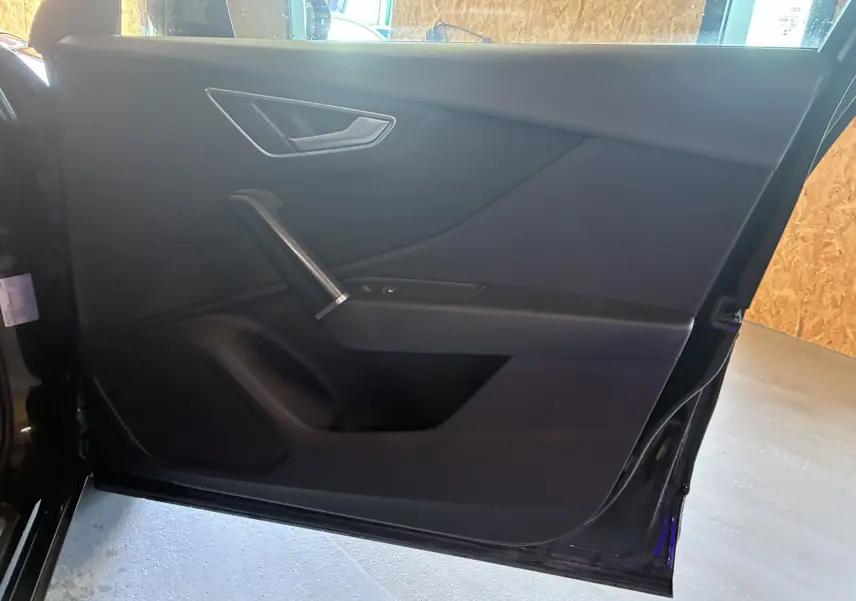 Vue intérieure de la porte arrière droite noire de l'Audi Q2 1.5 35 TFSI S-Line avec poignée argentée et panneau épuré.