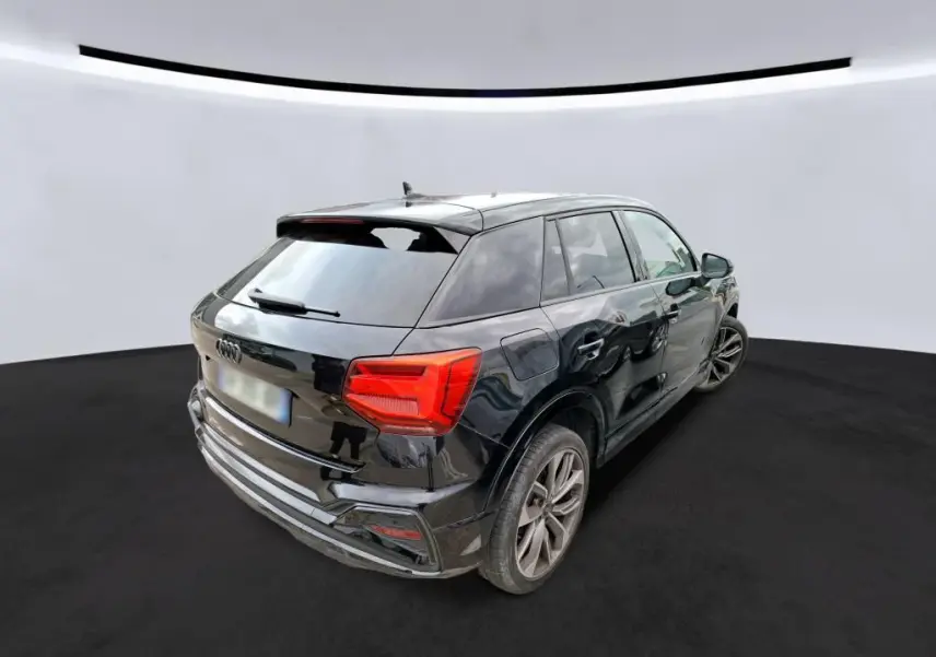 Audi Q2 noir en 3/4 avant droit, avec calandre noire et jantes alliage, stationné dans un garage moderne.