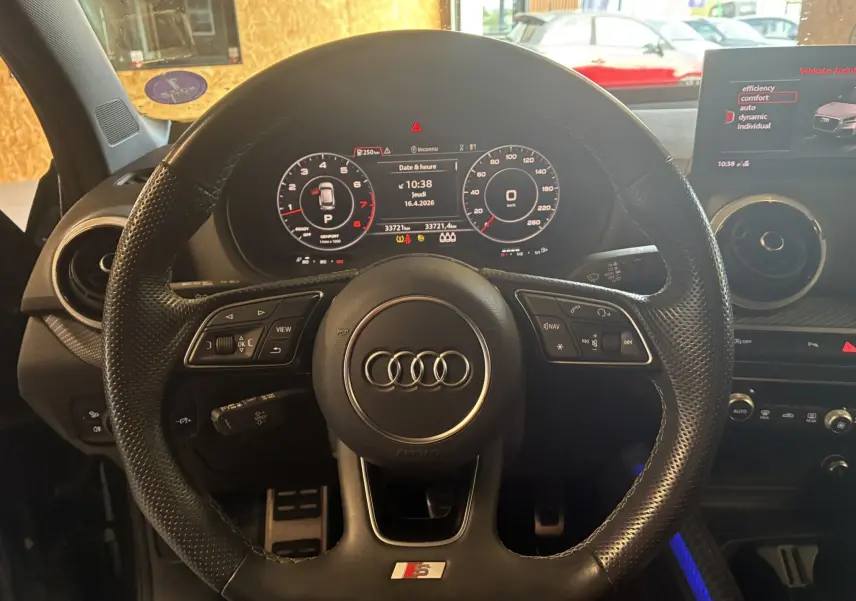 Vue rapprochée du volant sport noir perforé de l'Audi Q2 1.5 TFSI 2023 avec tableau de bord numérique et écran central.