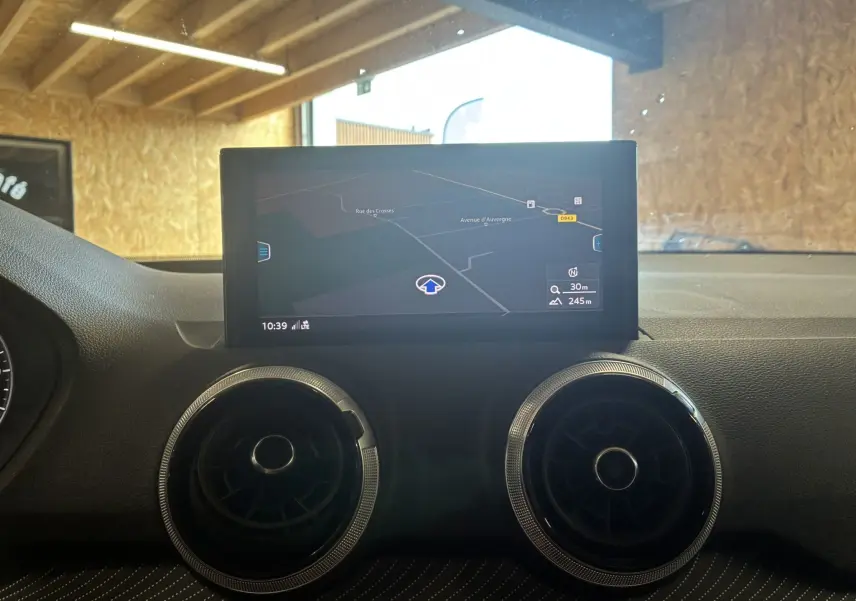Vue intérieure centrée sur l'écran GPS et les aérateurs ronds du tableau de bord de l'Audi Q2 noir 2023.