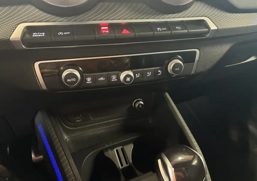 Vue rapprochée de la console centrale noire de l'Audi Q2 2023, avec commandes climatisation et éclairage d'ambiance bleu.