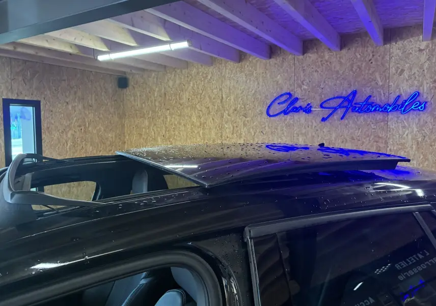 Toit ouvrant partiellement ouvert sur le côté gauche d'un Audi Q2 noir, intérieur et jantes visibles en arrière-plan.