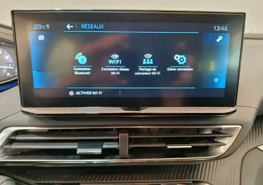 Écran tactile central affichant les options réseau Wi-Fi et Bluetooth, avec aérateurs et tableau de bord noir.