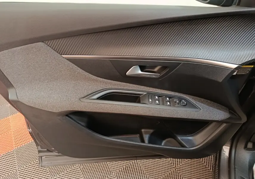 Vue intérieure côté gauche de la porte avant d’un Peugeot 3008 gris foncé avec commandes électriques des vitres et poignée argentée.