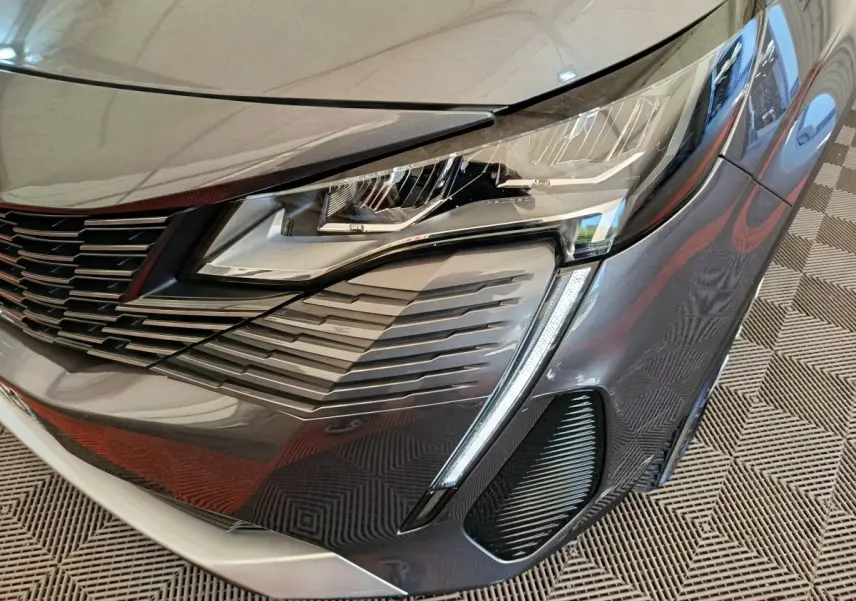 Gros plan sur le phare avant droit du Peugeot 3008 gris foncé, mettant en valeur la calandre et les feux LED distinctifs.