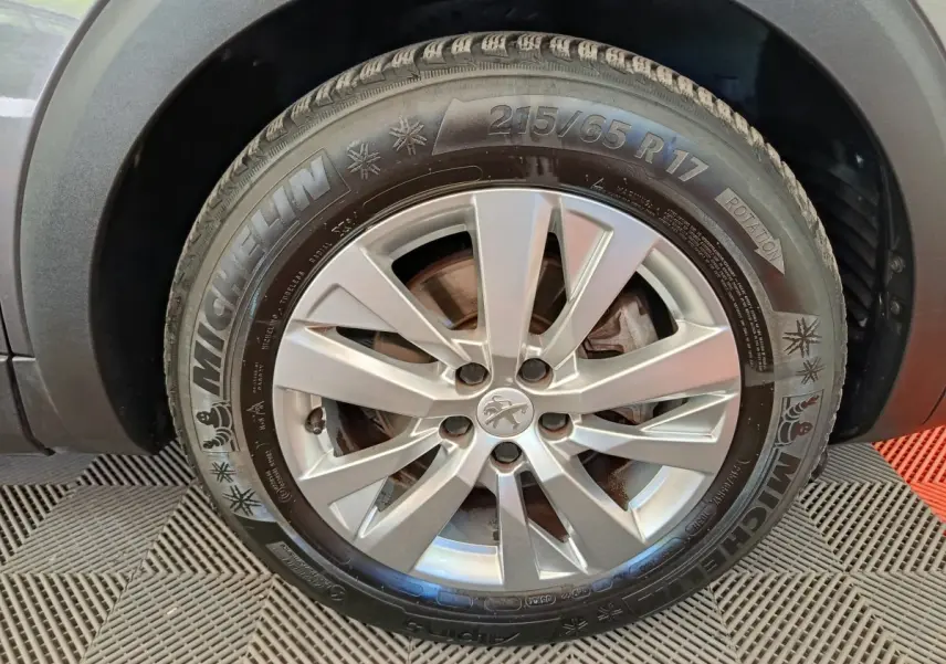 Gros plan sur la roue avant gauche d’un Peugeot 3008 gris foncé avec jante alliage et pneu Michelin hiver.