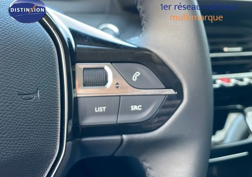 Détail du côté gauche du volant en cuir noir d'une Peugeot 208 Hybrid jaune, avec commandes audio intégrées.