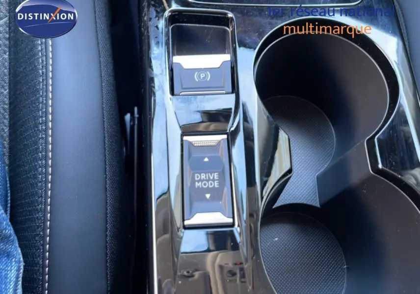 Gros plan sur la console centrale noire brillante avec boutons Drive Mode et frein à main électrique, porte-gobelets visibles.