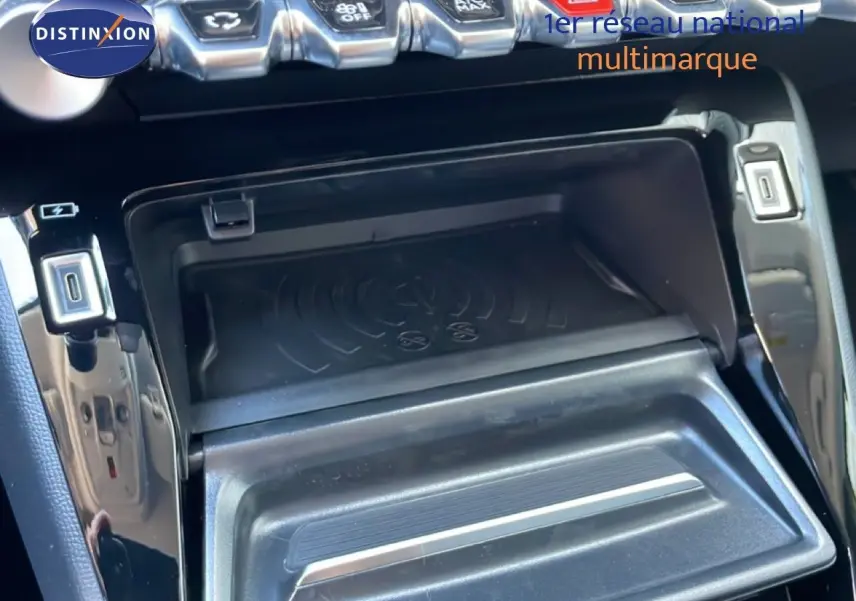 Gros plan sur la console centrale noire brillante de la Peugeot 208 Hybrid 110ch, montrant le chargeur sans fil et les commandes.