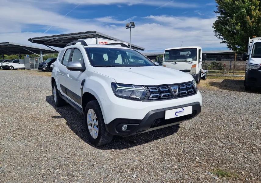 Dacia Duster blanc vue 3/4 avant droit, avec calandre noire et protections noires sur les bas de caisse.