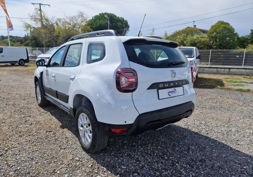 Vue 3/4 arrière droite d'un Dacia Duster blanc 2023 avec protections noires et jantes alliage 16 pouces.
