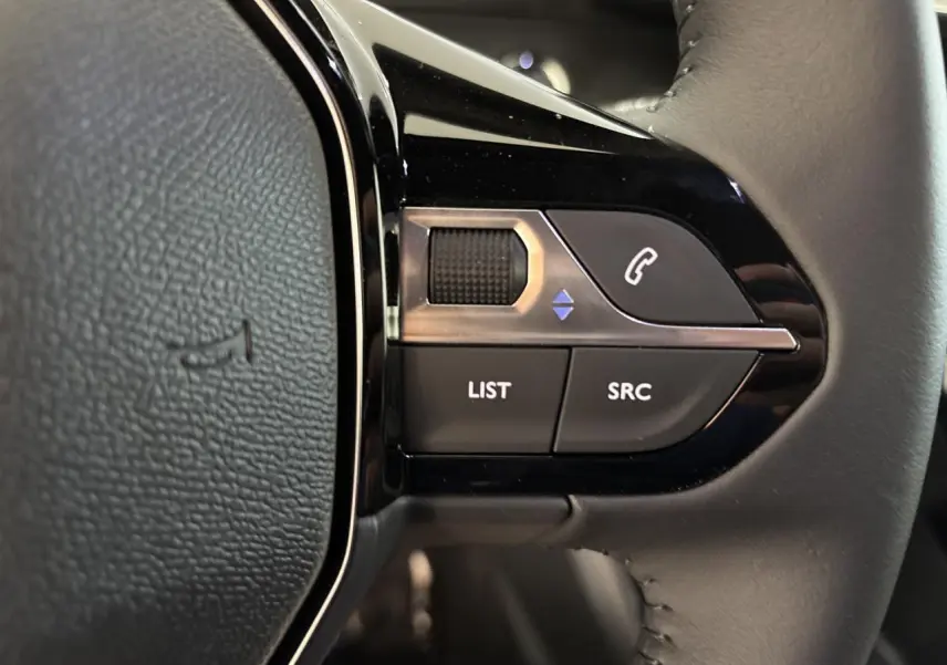 Gros plan sur les commandes multimédia noires et chrome intégrées au volant cuir gris du Peugeot 2008 hybride.