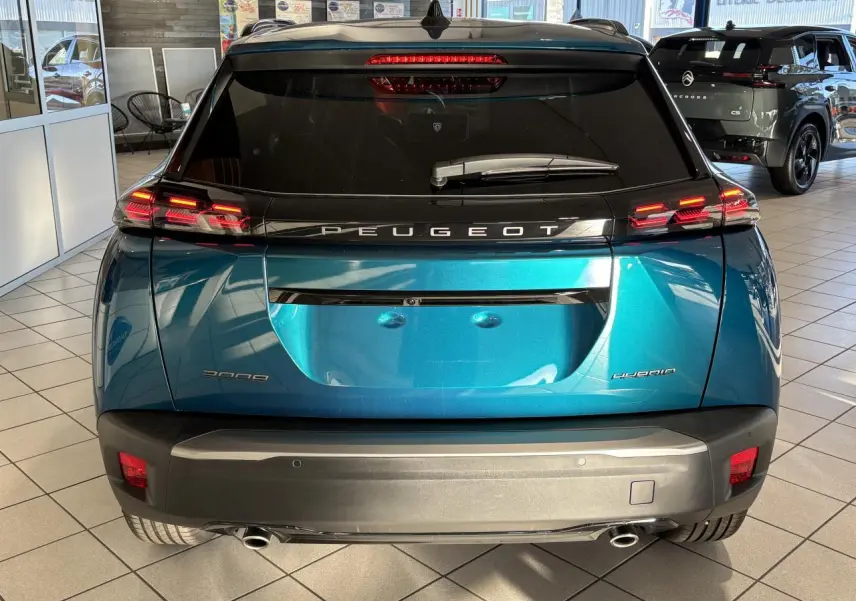 Vue arrière d'un Peugeot 2008 hybride bleu métallisé avec feux arrière LED en forme de griffes et double sortie d'échappement chromée.