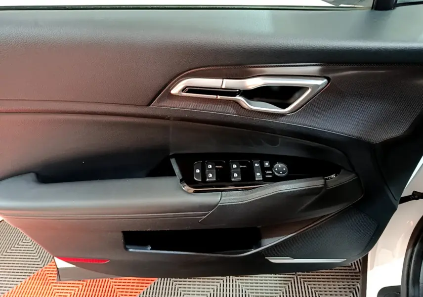 Gros plan sur la porte avant gauche blanche du Kia Sportage 2022 avec commandes électriques et poignée argentée.