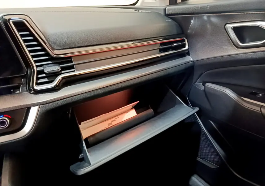 Vue intérieure côté passager du tableau de bord noir du Kia Sportage 2022 avec boîte à gants ouverte contenant des documents.