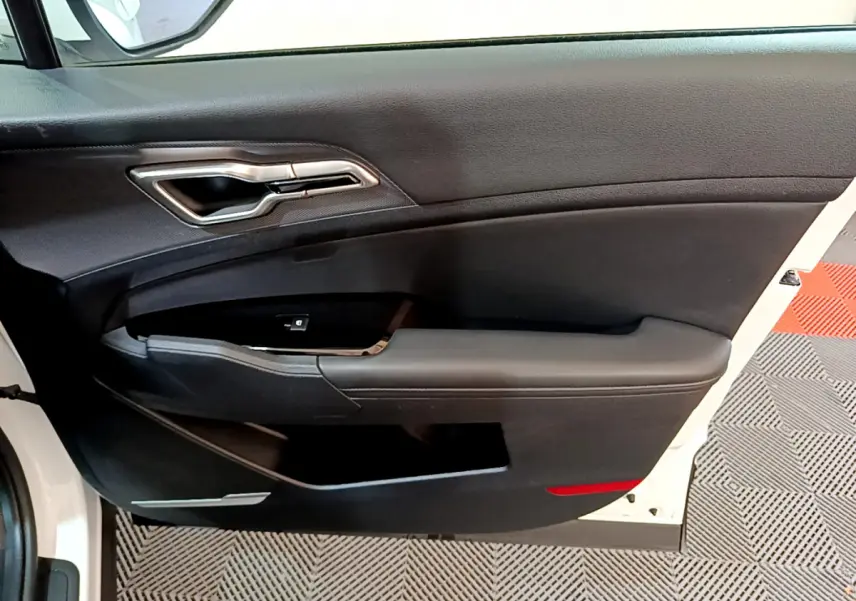 Intérieur côté gauche de la porte avant blanche du Kia Sportage 2022 avec poignée argentée et panneau noir.