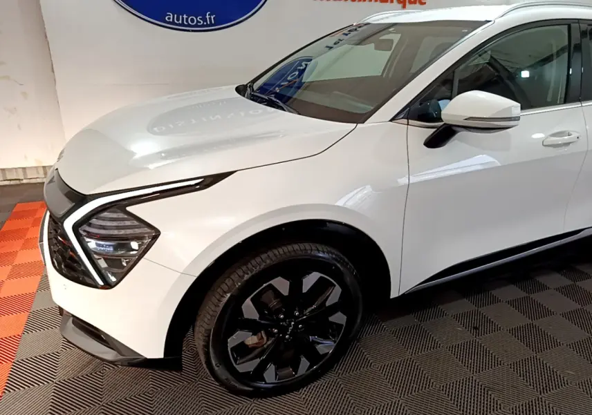 Vue 3/4 avant droit du KIA SPORTAGE blanc avec jantes noires et feux LED en forme de boomerang.