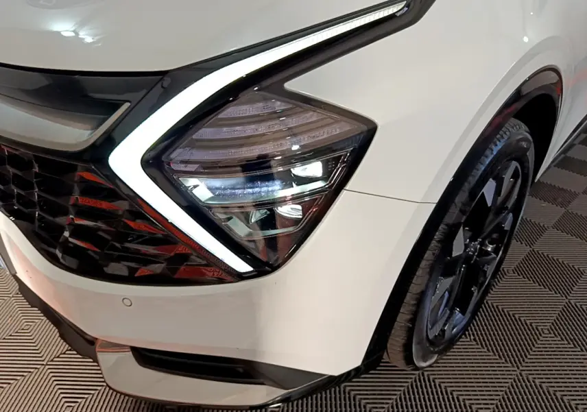 Gros plan sur le phare avant gauche blanc du Kia Sportage 2022 avec jante noire et éclairage LED distinctif.