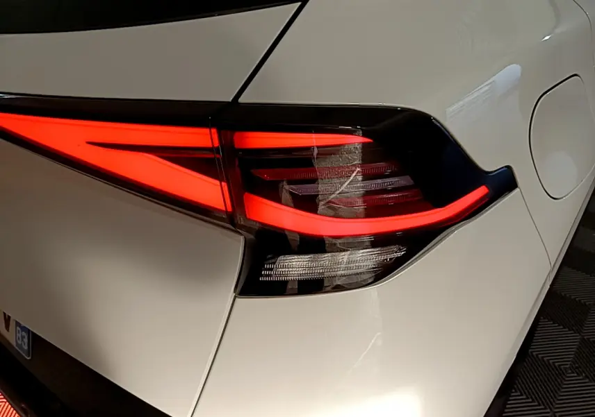 Gros plan sur le feu arrière droit rouge vif du KIA SPORTAGE blanc hybride rechargeable 2022, détail du coffre et trappe à carburant.