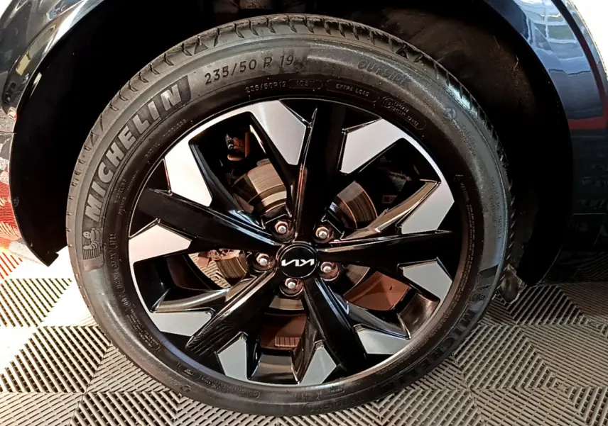 Gros plan sur la roue avant droite du KIA SPORTAGE blanc, jante alliage noir et argent avec logo KIA central.