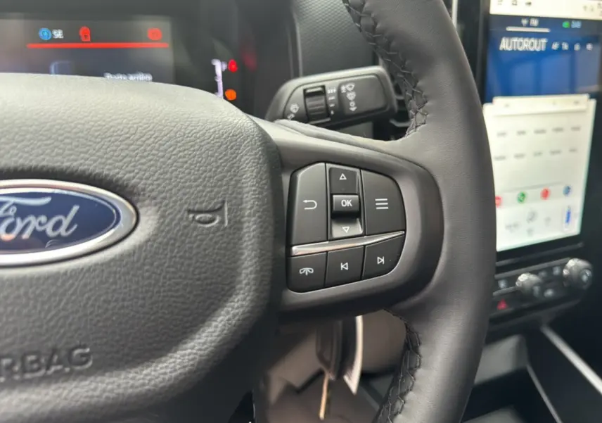 Gros plan sur le volant cuir multifonctions du Ford Ranger 2026 avec commandes au volant et écran tactile en arrière-plan.