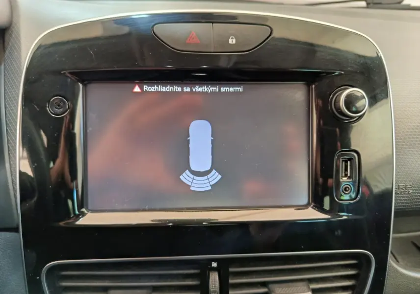 Écran tactile central affichant l'aide au stationnement arrière sur tableau de bord noir d'une Renault Clio Intens rouge.