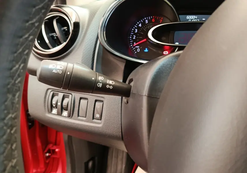 Vue intérieure côté gauche du volant de la Renault Clio rouge, avec commandes d'éclairage et tableau de bord partiel.