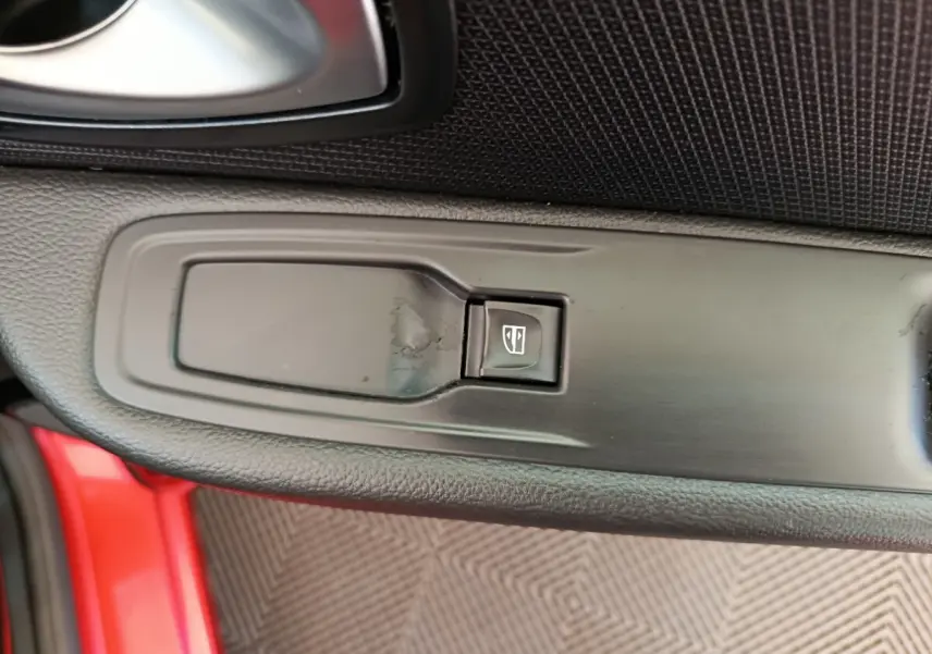 Gros plan sur le bouton de commande de la vitre électrique côté conducteur d’une Renault Clio rouge.