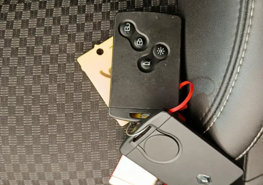 Gros plan sur les clés noires Renault posées sur un siège tissu noir à motifs, avec coutures blanches visibles.