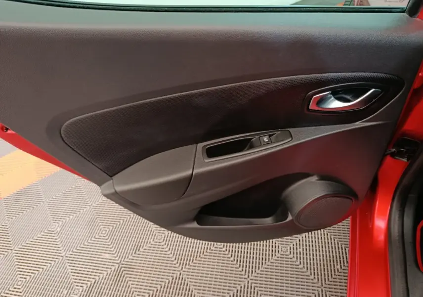 Vue rapprochée de la porte avant gauche rouge de la Renault Clio Intens 2018 avec commande de vitre et poignée intérieure.