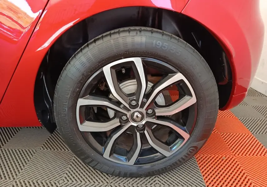 Gros plan sur la roue arrière droite de la Renault Clio rouge, mettant en valeur la jante alliage au design moderne.
