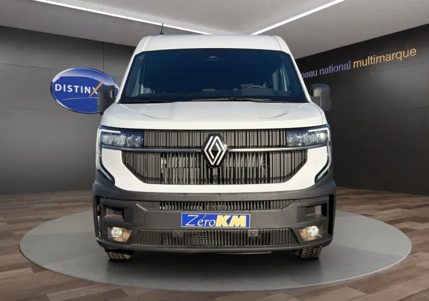 Vue frontale d’un Renault Master blanc avec calandre noire verticale et feux LED allumés en intérieur showroom.