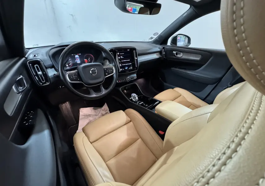 Intérieur du Volvo XC40 Recharge T5 2021 vu côté conducteur, sièges cuir beige et tableau de bord noir avec écran tactile central.