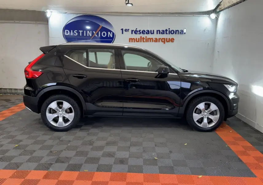 Profil côté gauche d'un Volvo XC40 Recharge T5 noir, avec jantes argentées, stationné en intérieur sur sol gris et orange.