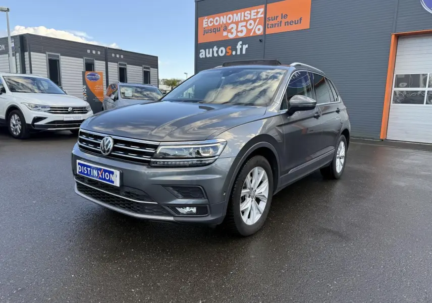 Volkswagen Tiguan gris Indium métallisé vu en 3/4 avant droit sur parking devant un bâtiment commercial.