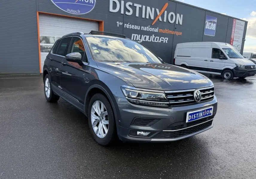 Volkswagen Tiguan gris Indium métallisé vu en 3/4 avant droit sur parking devant un bâtiment Distinxion.