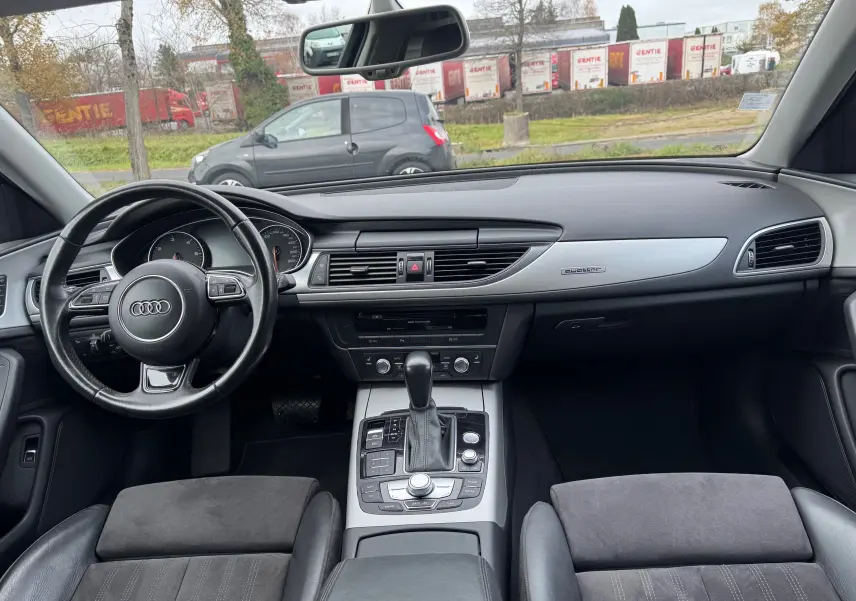 Vue intérieure avant de l’Audi A6 Avant 2015 noire, tableau de bord moderne avec console centrale et volant cuir multifonction.