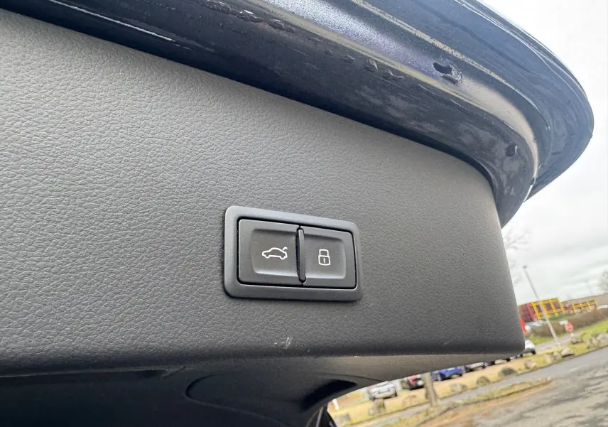 Gros plan sur les boutons d'ouverture et de verrouillage du hayon d'une Audi A6 Avant noire, vue depuis l'arrière avec hayon ouvert.