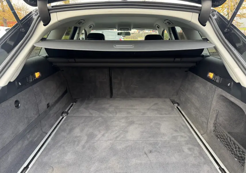 Coffre spacieux de l'Audi A6 Avant noir 2015 vu de l'arrière avec cache-bagages et éclairage latéral allumé.