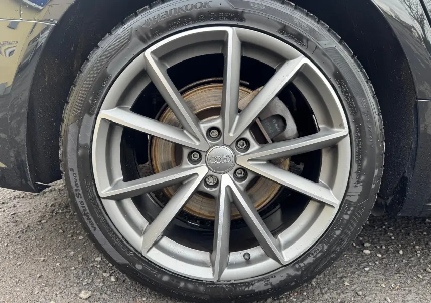 Gros plan sur la roue avant droite d’une Audi A6 Avant noire de 2015 avec jante alliage 19 pouces et logo Audi central.