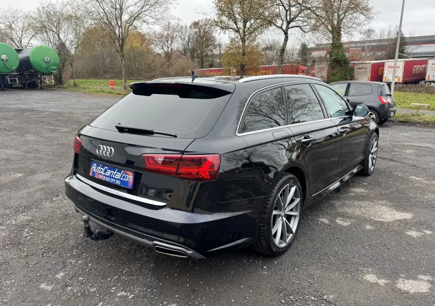Vue 3/4 arrière droite d'une Audi A6 Avant noire de 2015 avec jantes alliage et attelage de remorque visible.