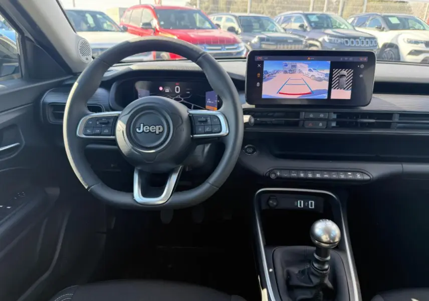 Vue intérieure frontale du Jeep Avenger 2025, tableau de bord noir avec volant multifonction et écran tactile affichant la caméra de recul.