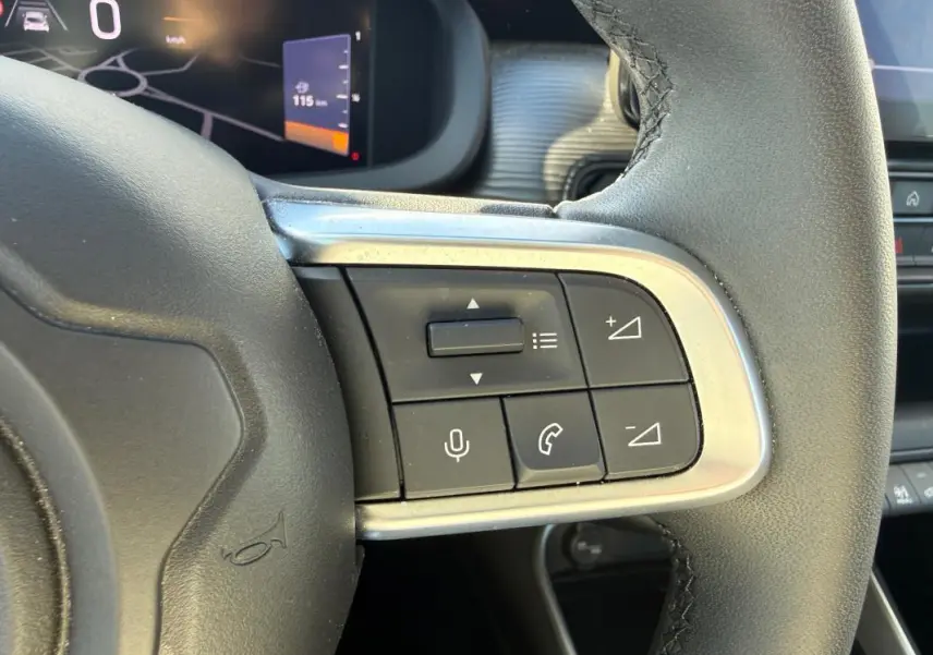 Gros plan sur les commandes au volant à droite du Jeep Avenger blanc, avec affichage numérique en arrière-plan.