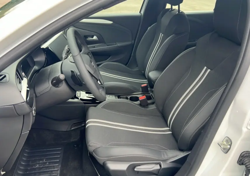 Vue intérieure côté conducteur de l’Opel Corsa blanc kontur, sièges noirs avec surpiqûres claires et volant multifonctions.