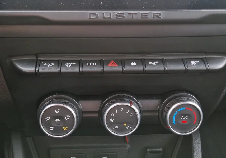 Gros plan sur la console centrale du Dacia Duster 2022 blanc, montrant les commandes de climatisation et les boutons de fonction.