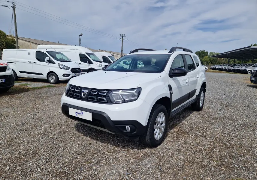 Dacia Duster blanc 4x4 vue 3/4 avant droit, avec protections noires sur les portières et jantes alliage 16 pouces.