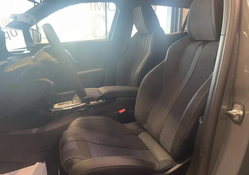 Vue intérieure côté conducteur du Peugeot 2008 gris, mettant en valeur les sièges sport en tissu et cuir avec surpiqûres contrastées.