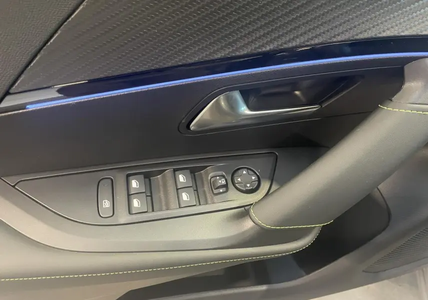 Détail de la porte avant gauche du Peugeot 2008 gris avec surpiqûres vertes et commandes de vitres électriques.